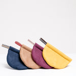 Four Ban Inoue pot holders (oven mitts) in different colours, each featuring a braided hanging cord. The holders are folded ovals, and stacked together horizontally to appear like semicircles. Colours from left to right: navy blue, brown, grape burgundy, yellow. Made in Japan and available at NiMi Projects UK.