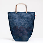 A large navy blue muslin Vegetable tote bag filled with onions, made in Japan by Ban Inoue using traditional mosquito net weaving techniques. The bag has a folded and stitched base for support and short top handles. On show at NiMi Projects UK.