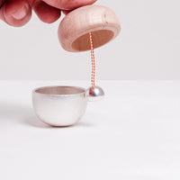 The Kuon Madoka acorn-shaped singing bowl chime in silver. The clapper is shown striking the bowl as a note is sounded. Designed by Yotsukawa Seisakusho for its Kisen brand, available at NiMi Projects in Sevenoaks, Kent.