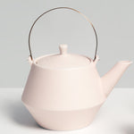 Brass-handled Japanese porcelain Frustum teapot in pinkish off white, placed on a pink Sunaolab trivet, available at NiMi Projects in the UK