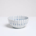 A side view of a white, Japanese porcelain, Mino-yaki, pinstriped bean-bowl dish, featuring a gently fluted edge and hairline thin radial lines in blue underglaze. Available at NiMi Projects UK.