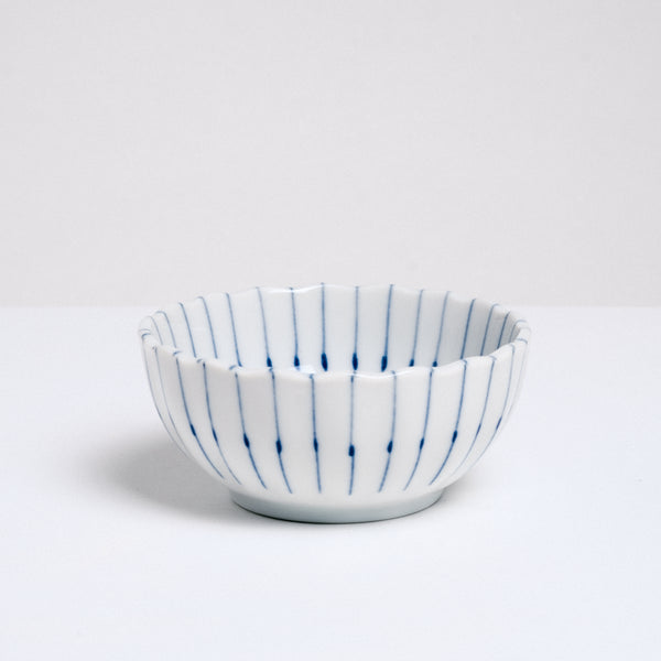 A side view of a white, Japanese porcelain, Mino-yaki, pinstriped bean-bowl dish, featuring a gently fluted edge and hairline thin radial lines in blue underglaze. Available at NiMi Projects UK.