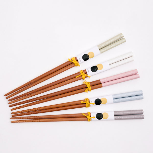 Five pairs of Japanese, wooden  chopsticks on show at NiMi Projects UK. Each pair of chopsticks have textured ends of grooves and are topped in different pastel colours. From top to bottom: Sage green, White, Pink, Blue and Grey.