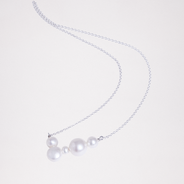 A pearl necklace on a silver chain, featuring five different sized spherical freshwater pearls joined together in a v-shape. Made by Japanese designers Onomatopee and available at NiMi Projects UK.