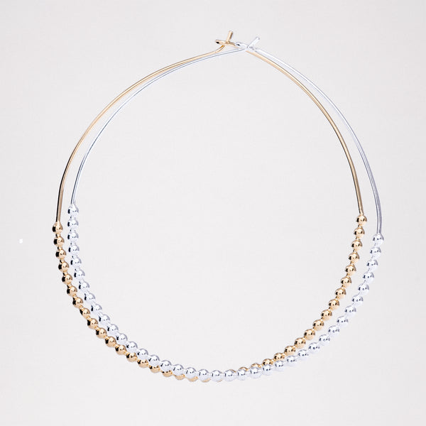 An image of silver and gold vermeil Onomatopee, large Puchipuchi Hoop Earrings, each 5 cm in diameter and featuring a row of tiny dots along the bottom section of the hoops. On show at NiMi Projects UK.