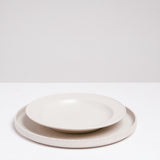 A side view of a Kihon no Utsuwa recycled porcelain side dish in white on top of a flat round plate by the same maker. Made in Japan and available at NiMi Projects UK.