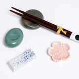 A group of four, different shaped, Japanese Mino-yaki, ceramic hashioki chopstick rests, made in Japan. Clockwise from top: a brown pebble shaped rest with a pair of wooden chopsticks, a pink sakura, cherry blossom rest, a white and blue specked pillow-shaped rest and a green sora-mame broad bean shaped rest. On show at NiMi Projects UK.