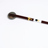 A brown pebble-shaped Japanese, Mino-yaki hashioki chopstick rest, with a pair of dark brown lacquered chopsticks. On show at NiMi Projects UK.