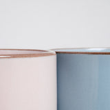 A detail image of the tops of two NiMi Projects’ Japanese ceramic Mino-yaki stacking mugs — one pink and one blue — placed side by side and showcasing each mug’s pastel satin glaze and unglazed lip.