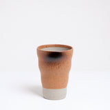 A Mino-yaki, Shigaraki style, Japanese pottery tumbler, featuring a raw clay base and a top glaze in a soft orange that is naturally speckled and singed during the firing process. Available at NiMi Projects UK.