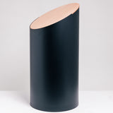 The cylindrical Moheim Swing Bin, medium size, in black, featuring a maple wood lid that sits on the top at a slant. Available at NiMi Projects UK