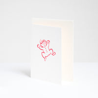 A congratulations card for a new baby at NiMi Projects UK, designed by Takako Copeland and featuring a red line drawing of a smiling baby in a romper suit. Inside the card is a white envelope. 