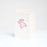 A congratulations card for a new baby at NiMi Projects UK, designed by Takako Copeland and featuring a red line drawing of a smiling baby in a romper suit. Inside the card is a white envelope. 