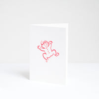 A congratulations card for a new baby, designed by Takako Copeland and featuring a red line drawing of a smiling baby in a romper suit. Available at NiMi Projects UK.