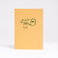  Letterpress printed in green on bright yellow, Takako Copeland's Oxalis Card features an illustration of a bundle of Oxalis growing tall as they are watered by a long-spout watering can.