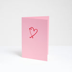 A standing pink card with a red line drawing illustration of a bird shaped as a heart by Takako Copeland. Available at NiMi Projects UK.