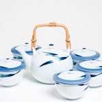 A vintage Japanese tea set in white porcelain, including a bamboo top-handled teapot and five lidded cups. The teapot features a design of bamboo leaves in a gradation of glaze of blue to green to white. Each of the cups has a lid with a wide blue rim and bamboo leaf details on the lid and side. Available at NiMi Projects UK.