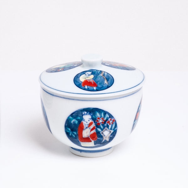 A large vintage white porcelain Japanese lidded tea cup, featuring a design of blue circles with illustrations of children playing in a garden. Available at NiMi Projects UK.