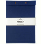 A French blue fabric-covered A4 Postalco Snap Pad, showing the two roundmetal snap clasps at its top and a white label wrapped around its center featuring the Postalco bird logo.