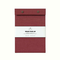 A rosewood red fabric-covered Postalco Snap Pad, showing the two roundmetal snap clasps at its top and a white label wrapped around its center featuring the Postalco bird logo.