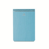 A top image of a Postalco A6 Note Book in powder blue, with a spiral top and featuring the Postalco bird logo debossed in gold.