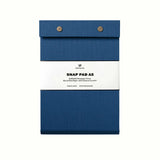 A lake blue pressed-cotton covered Postalco Snap Pad, showing the two roundmetal snap clasps at its top and a white label wrapped around its center featuring the Postalco bird logo.