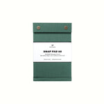 A dark green pressed-cotton covered A6 Postalco Snap Pad, showing the two roundmetal snap clasps at its top and a white label wrapped around its center featuring the Postalco bird logo.