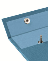 A detail image of the top left of a light  blue cotton-covered Postalco Snap Pad, showing a dusty blue interior textile and an open metal snap clasp.