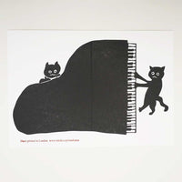 A letterpress printed greeting card by Takako Copeland, featuring a top view of a black grand piano and two black illustrated cats playing at its sides.