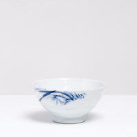 A Vintage 1940s Arita ware Japanese porcelain rice bowl, featuring textured sides and a motif of blue hand-painted grass brushstrokes. On display at NiMi Projects UK